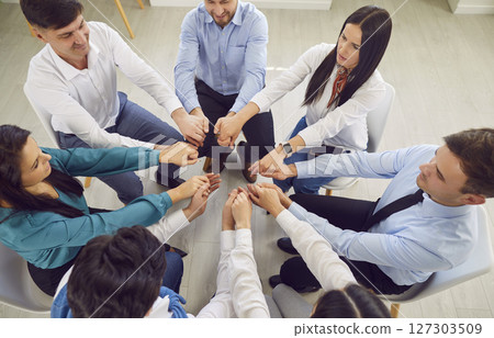 Top view of business people holding hands together sitting in a circle in office. 127303509