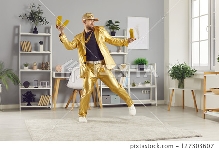 Funny young man holding gold bar having fun in living room at home celebrating success 127303607