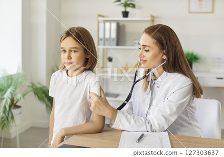 Pediatrician checking lung, heart of kid patient in clinic, female doctor, nurse holding stethoscope 127303637