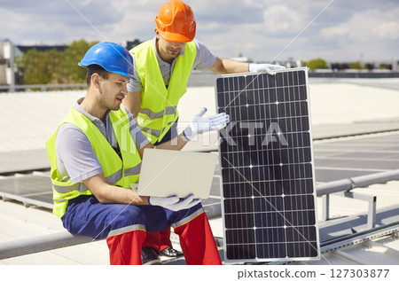 Repairmen Adjusting And Maintaining Solar Panels With Laptop On Roof 127303877