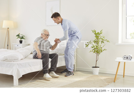 Doctor Or Nurse Assisting Elderly Patient Out Of Bed In Morning At Nursing Home Doctor Or Nurse Assisting Elderly Patient Out Of Bed In Morning At Nursing Home 127303882