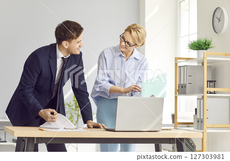 Two diverse office businesspeople chatting standing near laptop, sharing new ideas or startup  127303981