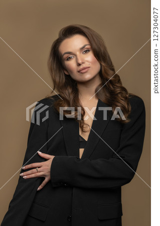 Woman with long wavy hair and black suit studio portrait on beige background 127304077
