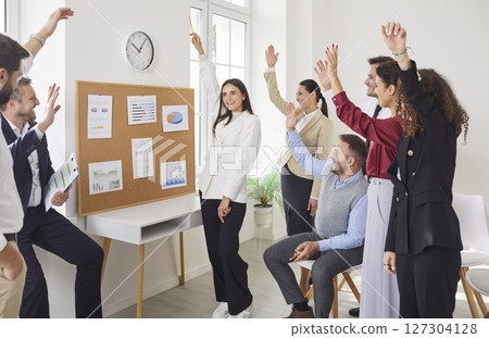 Young cheerful company employees raising hands to vote at the conference standing in meeting room. Young cheerful company employees raising hands to vote at the conference standing in meeting room. 127304128