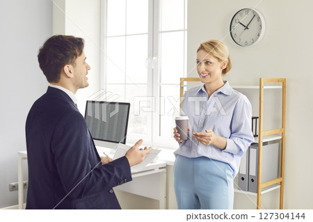 Smiling colleagues discussing work project in office, enjoying conversation during coffee break. 127304144