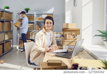Woman working in warehouse checking stock and inventory with male coworker. 127304162