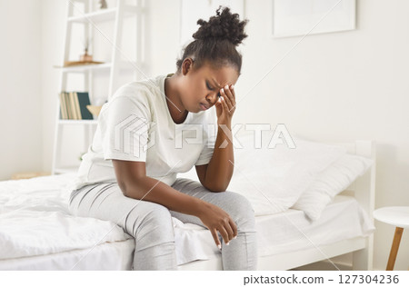 Sad African American Woman Suffering From A Headache Or Migraine After Waking Up Sad African American Woman Suffering From A Headache Or Migraine After Waking Up 127304236