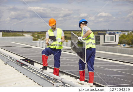 Repairmen are maintaining and installing solar panels on a rooftop. 127304239