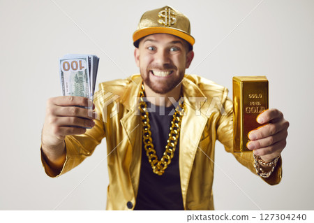 Funny young man in golden suit holding money cash and gold bar on white studio background. 127304240