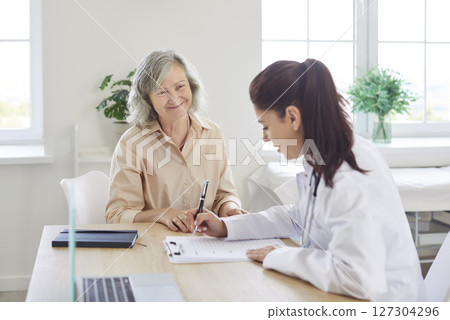 Physician writing out a prescription for her happy, smiling, senior woman patient Physician writing out a prescription for her happy, smiling, senior woman patient 127304296