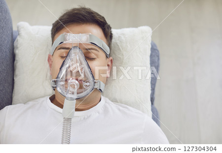 Man with pneumonia or bronchitis wearing an oxygen mask lying on the sofa at home 127304304