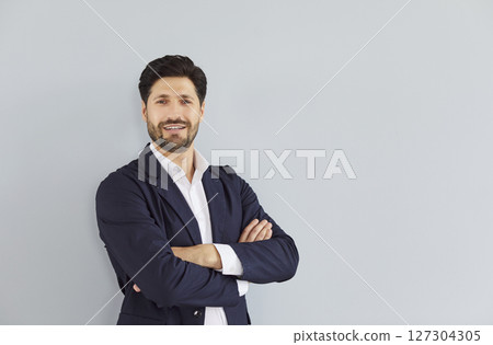 Portrait of confident bearded young business man on grey wall background. 127304305