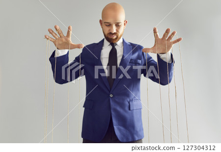 Man in suit pulling strings of puppet. 127304312