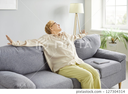 Mature peaceful woman in casual clothes sitting on comfortable sofa resting at home Mature peaceful woman in casual clothes sitting on comfortable sofa resting at home 127304314