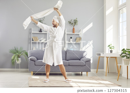 Happy, funny man in a white bathrobe and towel relaxing and having fun after shower Happy, funny man in a white bathrobe and towel relaxing and having fun after shower 127304315
