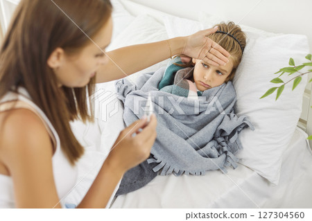 Caring kind young affectionate mom and sick child in bed measuring temperature, touching forehead Caring kind young affectionate mom and sick child in bed measuring temperature, touching forehead 127304560
