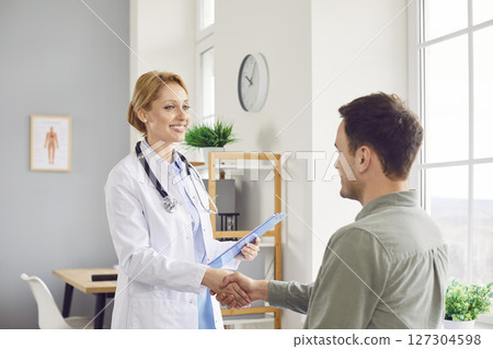 Friendly doctor shaking hands with a young patient standing in medical clinic Friendly doctor shaking hands with a young patient standing in medical clinic 127304598