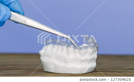 gloved hand using tweezers to adjust a clear dental aligner on a plaster teeth model for orthodontic fitting gloved hand using tweezers to adjust a clear dental aligner on a plaster teeth model for orthodontic fitting 127304628