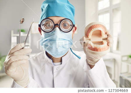 Funny doctor dentist with dental tools and jaws in medical uniform at work in dentistry clinic Funny doctor dentist with dental tools and jaws in medical uniform at work in dentistry clinic 127304669