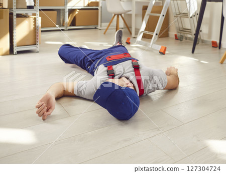 Close up of male worker storekeeper in overall lying unconscious on the floor in warehouse. Close up of male worker storekeeper in overall lying unconscious on the floor in warehouse. 127304724