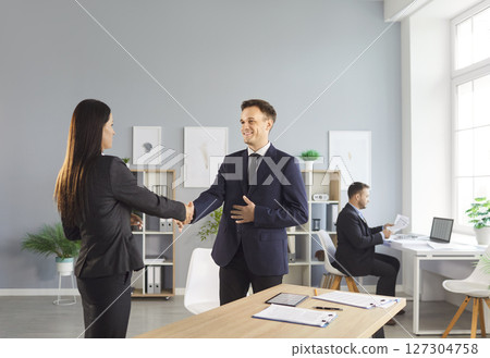 Man and woman standing in office making deal shaking hands celebrating business achievement. 127304758