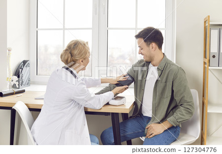 Female doctor therapist measuring blood pressure of male patient in medical clinic. Female doctor therapist measuring blood pressure of male patient in medical clinic. 127304776