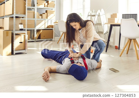 Woman giving first aid to Injured unconscious worker lying on the floor on workplace in warehouse 127304853
