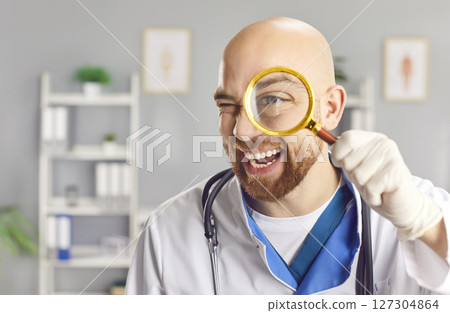Cheerful doctor is seen winking and smiling broadly while holding magnifying glass up to his eye. 127304864