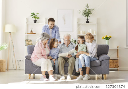 Big happy family sitting on sofa at home looking through a photo album enjoying good memories Big happy family sitting on sofa at home looking through a photo album enjoying good memories 127304874