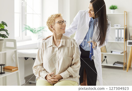 Smiling female doctor in white coat standing next to patient, offering support during consultation. Smiling female doctor in white coat standing next to patient, offering support during consultation. 127304923