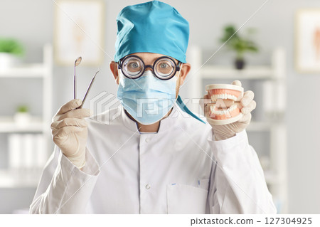 Funny doctor dentist with dental tools and jaws in medical uniform at work in dentistry clinic 127304925