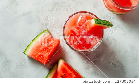 Top view of refreshing watermelon mocktail with ice cubes and fruit garnish on white textured background, vibrant pink drink with juicy slices around, light and clean presentation, summer refreshment 127305034