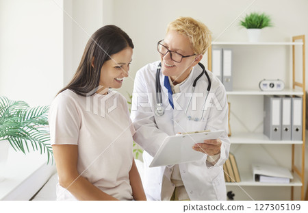 Positive happy practitioner female doctor showing clip board paper test to patient woman, explaining Positive happy practitioner female doctor showing clip board paper test to patient woman, explaining 127305109