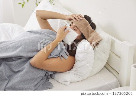 Sick young woman with fever lying in bed, sneezing in tissue, suffering from cold, infection or flu. Sick young woman with fever lying in bed, sneezing in tissue, suffering from cold, infection or flu. 127305205
