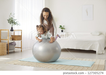 Happy mother and little daughter having fun and playing with exercise ball at home Happy mother and little daughter having fun and playing with exercise ball at home 127305274