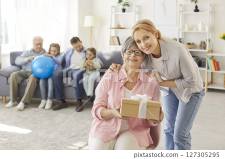 Excited senior grandmother, granny holding birthday present together with adult daughter 127305295