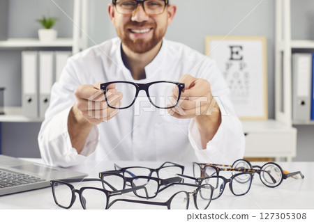 Ophthalmologist showing glasses, smiling doctor in clinic, helping to choose correct medical vision  127305308