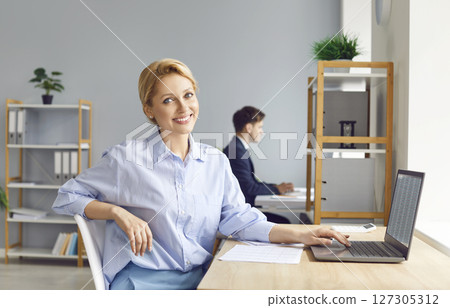 Happy smiling business woman accountant working on a laptop with at office and looking at camera. 127305312