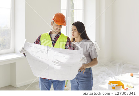Foreman worker and female client watching flat plan to supervise, direct, worker looking at project Foreman worker and female client watching flat plan to supervise, direct, worker looking at project 127305341