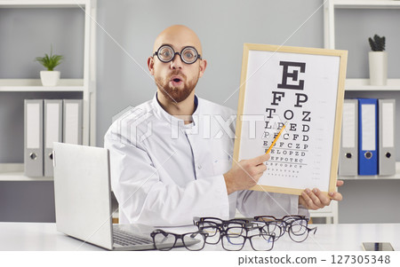 Funny optician male doctor checking a patient's vision sitting at desk in ophthalmology clinic. 127305348