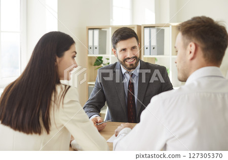 Financial advisor consulting a young confident couple about insurance sitting at desk in office. 127305370