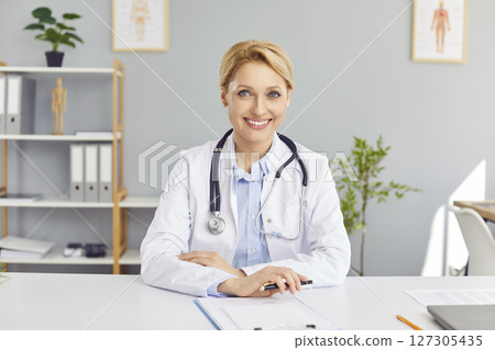 Portrait of cheerful young friendly female doctor in white medical uniform looking at camera. Portrait of cheerful young friendly female doctor in white medical uniform looking at camera. 127305435