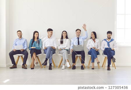 Portrait of happy smiling young man raising hand to ask or answer a question on a business meeting. 127305436