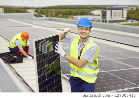 Two men are working on installing solar panels on the roof of a building. 127305438
