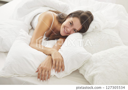 Happy young girl lying on bed in bedroom wearing sleepwear waking up in the morning. Happy young girl lying on bed in bedroom wearing sleepwear waking up in the morning. 127305534