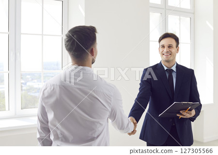 Man realtor agent standing in new apartments with signed contract shaking hands with customer 127305566