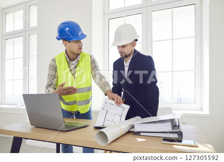 Two male contractors in hard hats discuss the master plan in a room Two male contractors in hard hats discuss the master plan in a room 127305592