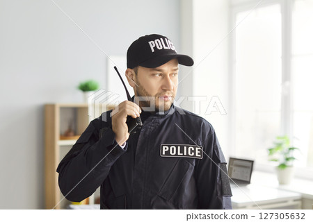 Portrait of confident police officer standing indoors and holding walkie talkie in hands. 127305632