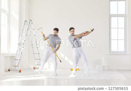 Team of house painters having fun with paint rollers painting the wall of new apartment. Team of house painters having fun with paint rollers painting the wall of new apartment. 127305633