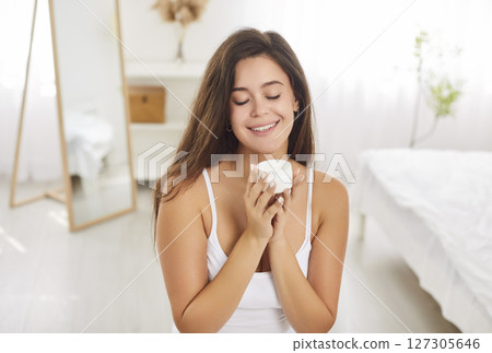 Attractive young woman holding cream, satisfied with professional cosmetic product results, happy  127305646